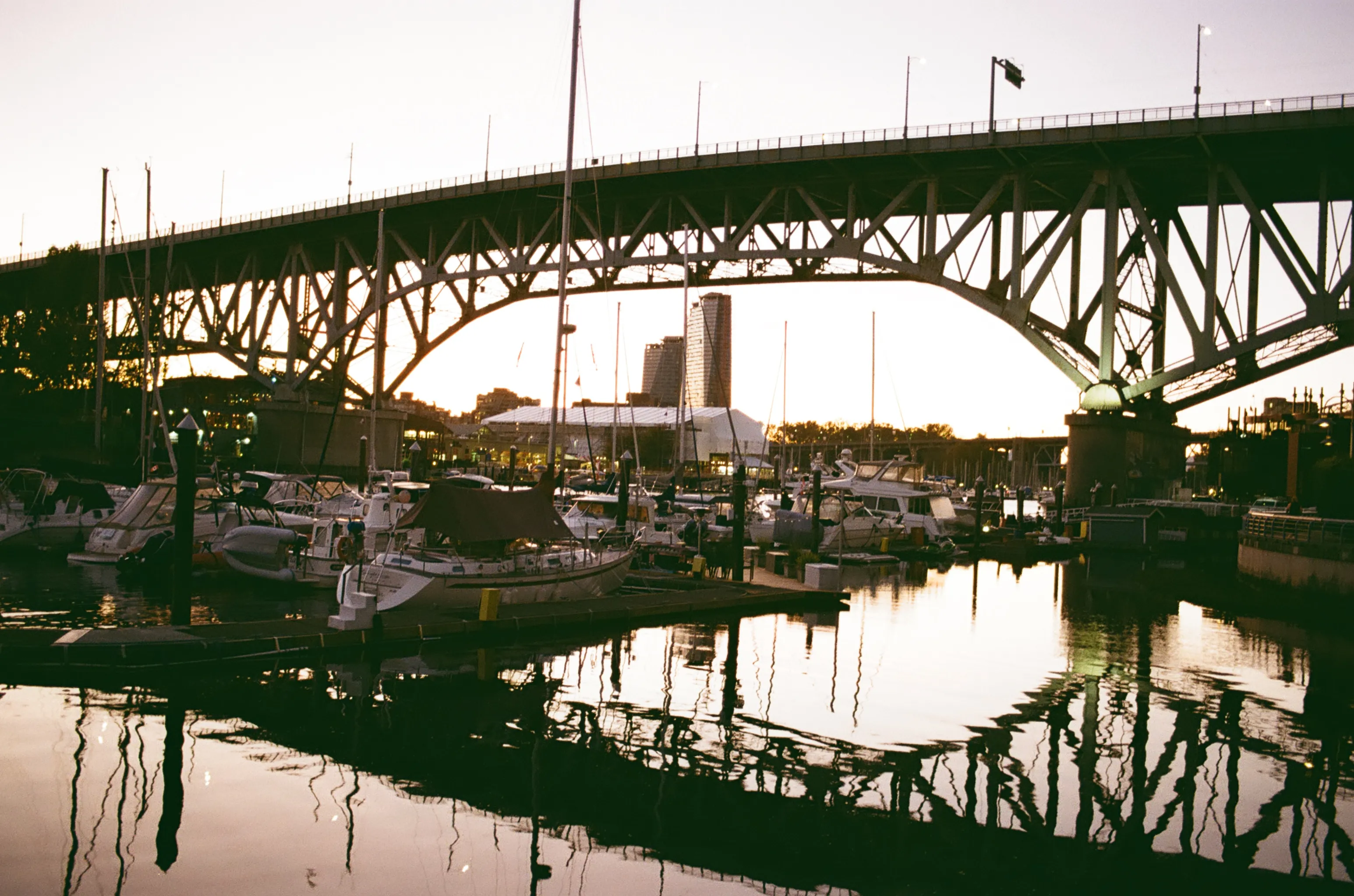 Bridge arching over a Vancouver marina at sunset, with boats moored below